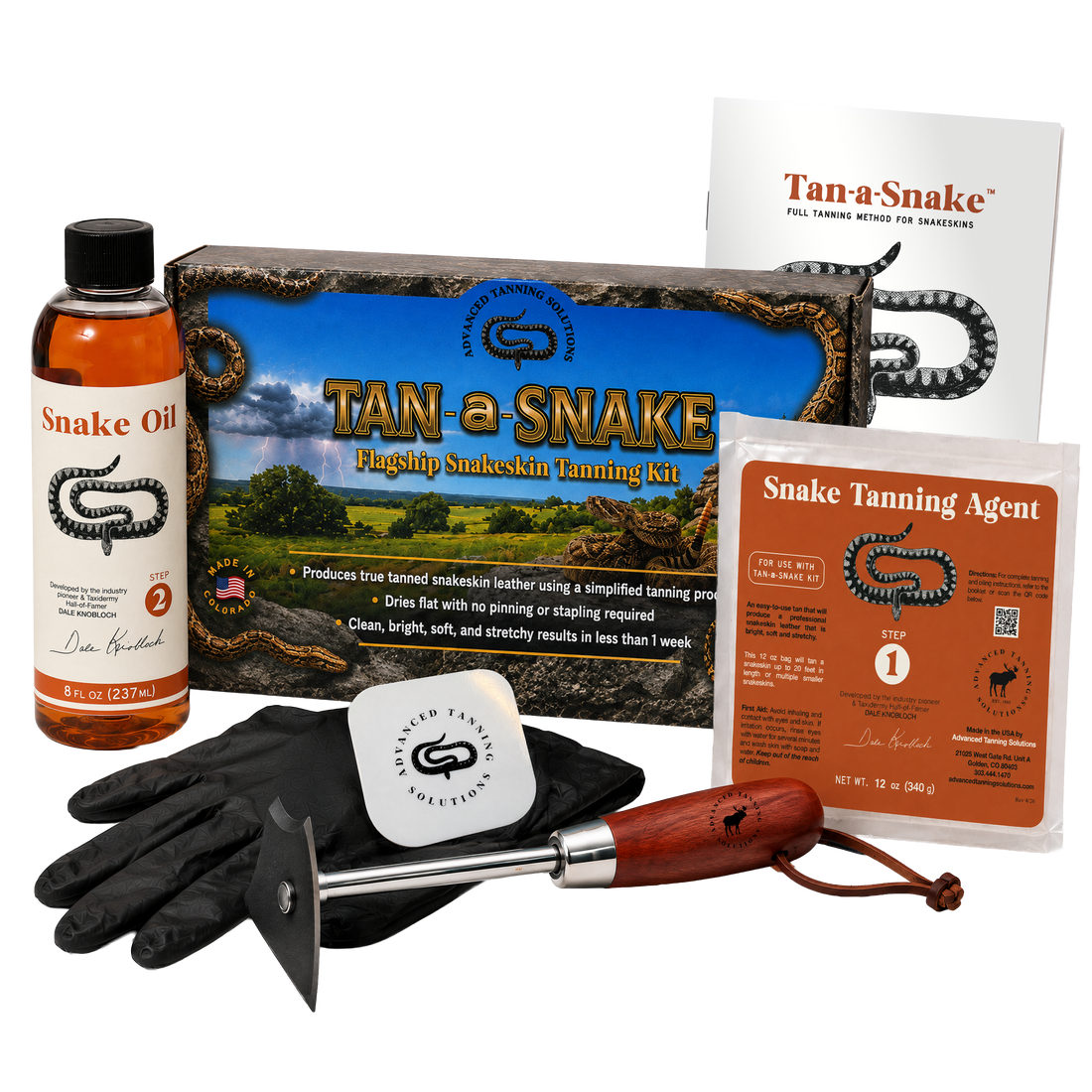 Tan-a-Snake  snake skin tanning kit with black rubber gloves, wooden-handled fleshing tool, tan-a-Snake box, bottle of snake oil, bag of snake tanning agent, and an instruction booklet