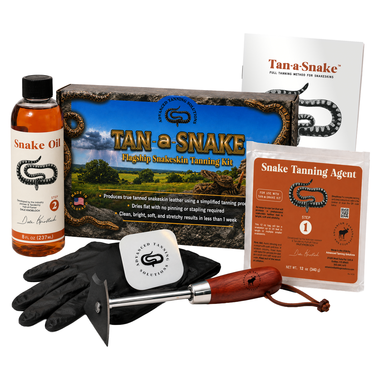 Tan-a-Snake  snake skin tanning kit with black rubber gloves, wooden-handled fleshing tool, tan-a-Snake box, bottle of snake oil, bag of snake tanning agent, and an instruction booklet