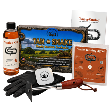 Tan-a-Snake  snake skin tanning kit with black rubber gloves, wooden-handled fleshing tool, tan-a-Snake box, bottle of snake oil, bag of snake tanning agent, and an instruction booklet